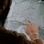 Close-up of a person's hand pointing at a map inside a car, emphasizing travel.
