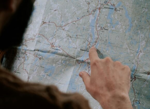 Close-up of a person's hand pointing at a map inside a car, emphasizing travel.